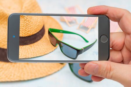 Travel set - sunglasses, straw hat. Photo smartphone. Smartphone in hand.の写真素材