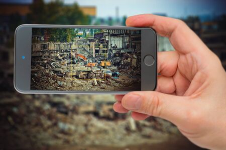 Destroyed industrial enterprise. Photos of a smartphone. Smartphone in hand. Excavator on the...