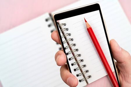 Red pencil and paper notebook on smartphone screen.の写真素材