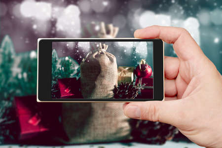 Christmas composition on the smartphone screen. Holiday gifts bag. Gift boxes and bump.