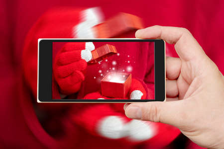 Christmas gift box on the smartphone screen. Festive composition. Red background.の写真素材