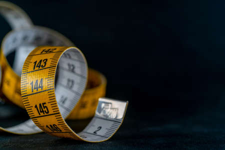 Yellow measuring tape on a dark background.の写真素材