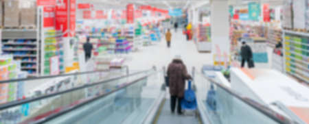 Blurred escalator in a supermarket. Selling goods in a retail store. Blurred background of customers in medical masks in a store.の写真素材