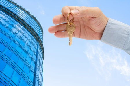 Apartment key in a man's hand. Brass house door lock key. Modern building, view from below. Architecture in modern city.の写真素材