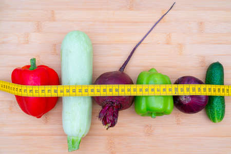 Yellow measuring tape and vegetables on a wooden cutting board. Healthy lifestyle diet.の写真素材