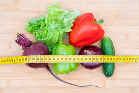 Yellow measuring tape and vegetables on a wooden cutting board. Healthy lifestyle diet.の写真素材