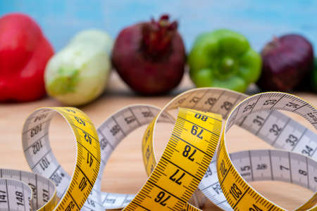 Yellow measuring tape and vegetables on a wooden cutting board. Healthy lifestyle diet.の写真素材