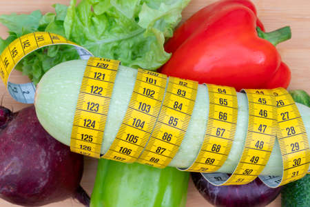 Yellow measuring tape and vegetables on a wooden cutting board. Healthy lifestyle diet.