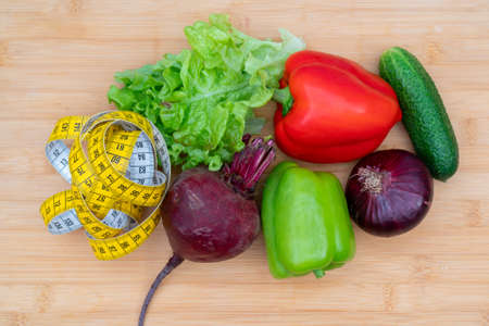 Yellow measuring tape and vegetables on a wooden cutting board. Healthy lifestyle diet.の写真素材
