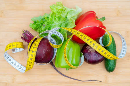 Yellow measuring tape and vegetables on a wooden cutting board. Healthy lifestyle diet.の写真素材