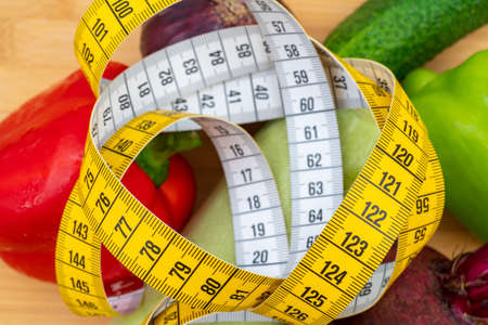 Yellow measuring tape and vegetables on a wooden cutting board. Healthy lifestyle diet.の写真素材