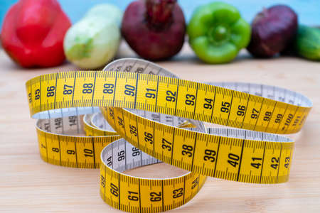 Yellow measuring tape and vegetables on a wooden cutting board. Healthy lifestyle diet.の写真素材