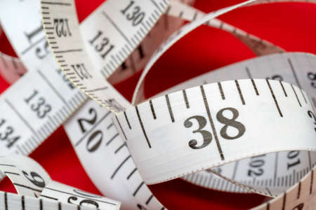 White measuring tape on red background. Measurement of length and circumference. Lose weight and get fat.の写真素材