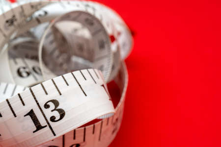 White measuring tape on red background. Measurement of length and circumference. Lose weight and get fat.の写真素材