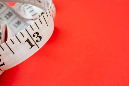 White measuring tape on red background. Measurement of length and circumference. Lose weight and get fat.の写真素材