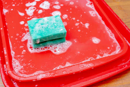 Disinfection of red plastic food tray in fast food. Washing the tray with a sponge and soap.の写真素材