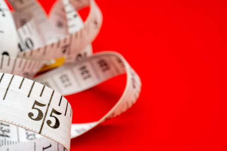 White measuring tape on red background. Measurement of length and circumference. Lose weight and get...