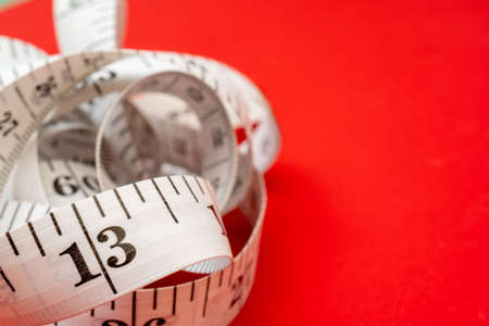 White measuring tape on red background. Measurement of length and circumference. Lose weight and get fat.の写真素材