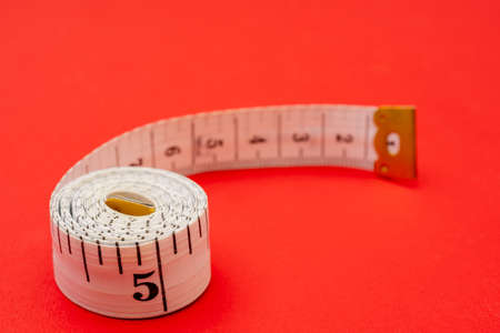 White measuring tape on red background. Measurement of length and circumference. Lose weight and get fat.の写真素材