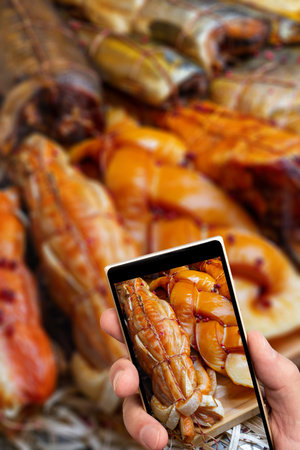 Smoked fish on smartphone screen. Selling seafood in a supermarket. Delicious delicacy fish for a festive table.の写真素材