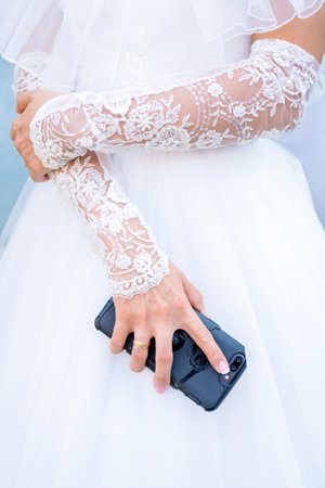 The bride in a white dress holds a smartphone in her hand.の写真素材