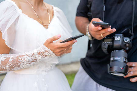 The bride in a white dress holds a smartphone in her hand.の写真素材