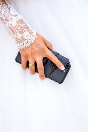 The bride in a white dress holds a smartphone in her hand.の写真素材