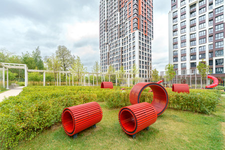 A park with a red sculpture and benches. The park is surrounded by buildings. The sculpture and benches are red and are placed in the grass.の写真素材