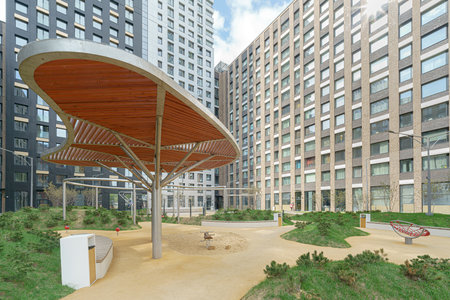 A park with a wooden pavilion and benches. The pavilion is covered in wood and has a curved roof. The park is surrounded by buildings, with one of them being a large apartment building.の写真素材