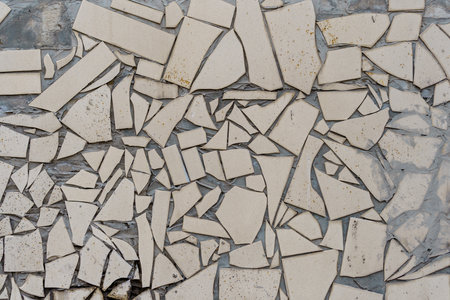 A wall with many pieces of broken tiles. The wall is white. The tiles are broken in different shapes and sizes.の写真素材