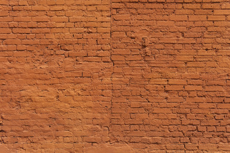 A textured red brick wall bears the marks of time and history urban. Its warm hue and rough surface evoke a sense of nostalgia, craftsmanship, and industrial charm.の写真素材