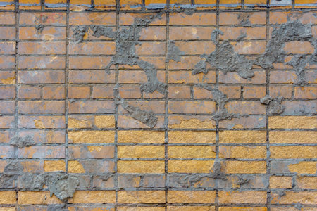 A yellow brick wall is marked with irregular splashes of cement. The rough contrast adds an unfinished, industrial character.の写真素材