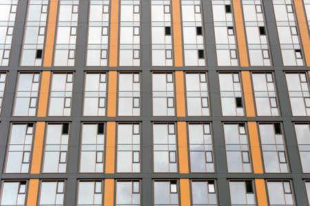 A modern building facade features vertical orange and gray panels with grid-like windows. The...