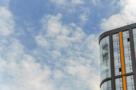 A modern building with glass and orange panels rises against a partly cloudy sky. The sleek...