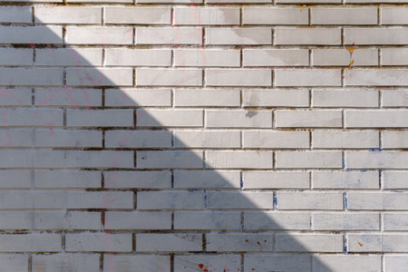 A white brick wall with horizontal rows is partially covered by a diagonal shadow. The contrast between light and dark areas emphasizes the structure and alignment of the bricks.の写真素材