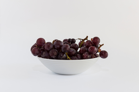 Red grapes on a white bowl, and white backgroundの写真素材