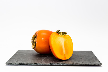 Two Persimmon's in a Slate Board Isolated on a White Backgroundの写真素材