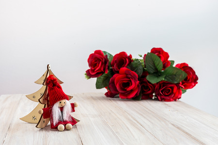 Christmas Elf Sitting Across a Christmas Tree and a Roses Bouquet in The Backの写真素材