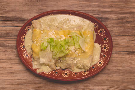 Traditional Mexican Food; Green enchiladas, in a clay plate on a wooden table.の写真素材