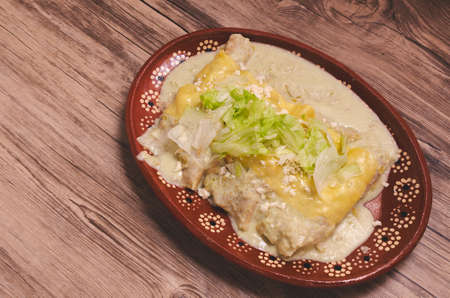 Traditional Mexican Food; Green enchiladas, in a clay plate on a wooden table.の写真素材