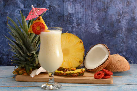 Pina colada, tropical cocktail. Glass of piÃ±a colada on a blue wooden table with the components of the cocktail in the background.の写真素材
