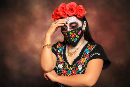 Catrina with embroidered mask. Young woman made up as a catrina for the Day of the Dead celebration with a colorful hand-embroidered mask.の写真素材