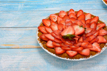 Cheesecake decorated with fresh strawberries on a blue wooden table.の写真素材