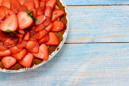 Cheesecake decorated with fresh strawberries on a blue wooden table.の写真素材