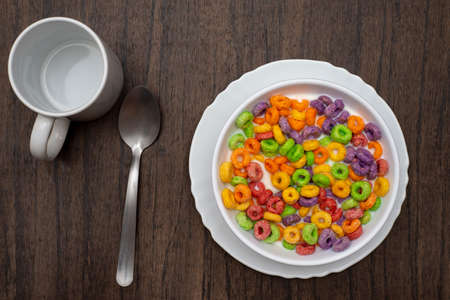 White bowl with cereal in the form of colored rings on wooden table. Breakfast cereal.