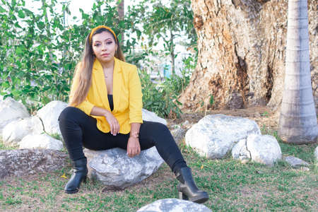 Outdoor portrait of woman in yellow jacket. Portrait of young Mexican woman in a garden at sunset.