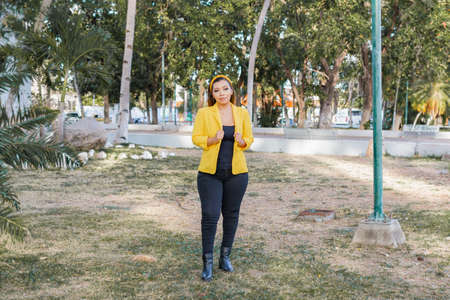 Outdoor portrait of woman in yellow jacket. Portrait of young Mexican woman in a garden at sunset.の写真素材