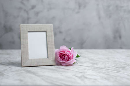 Picture frame portrait on marble table with a rose on one side. Mockup.の写真素材