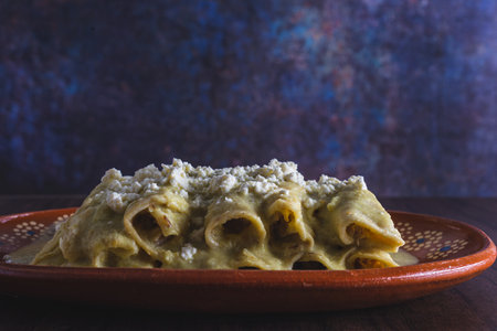 Green Enchiladas served in a clay dish on a wooden table. Typical Mexican food. Colorful background.
