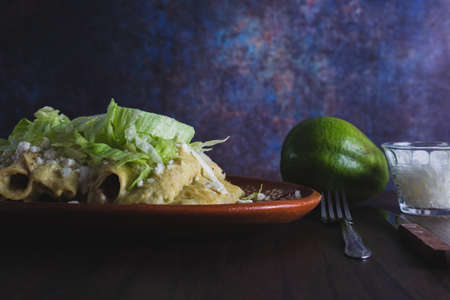 Green Enchiladas with lettuce served in a clay dish on a wooden table.の写真素材